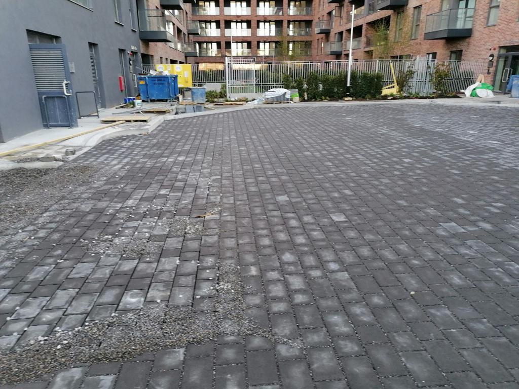 A cobblestone street under construction with a building and a fence